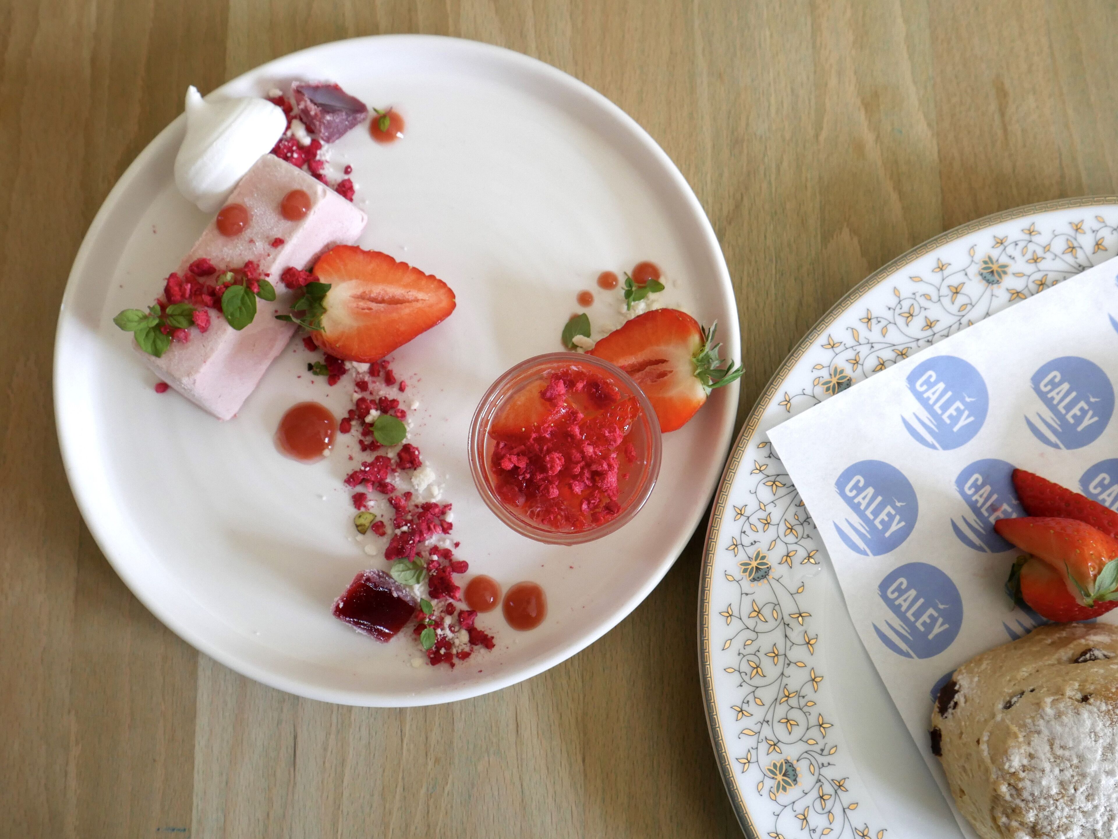 Un plato de postre con fresas, una porción de helado y un recipiente pequeño de salsa de frambuesa.