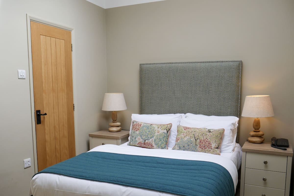 A bedroom with a bed, two bedside tables, a nightstand, a door, and a wall-mounted headboard.