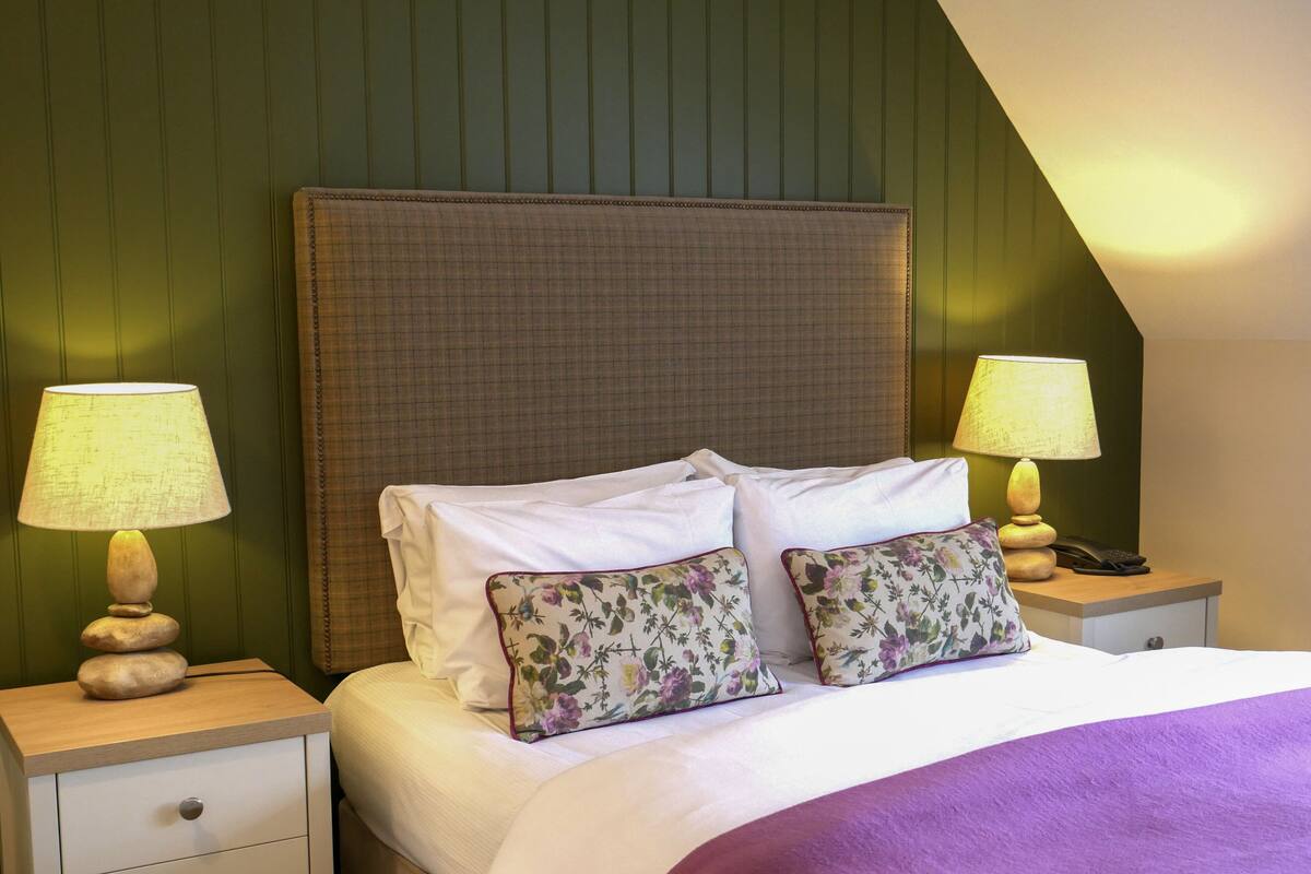 A neatly made bed with white linens and two floral pillows, flanked by two bedside tables with lamps and a phone.