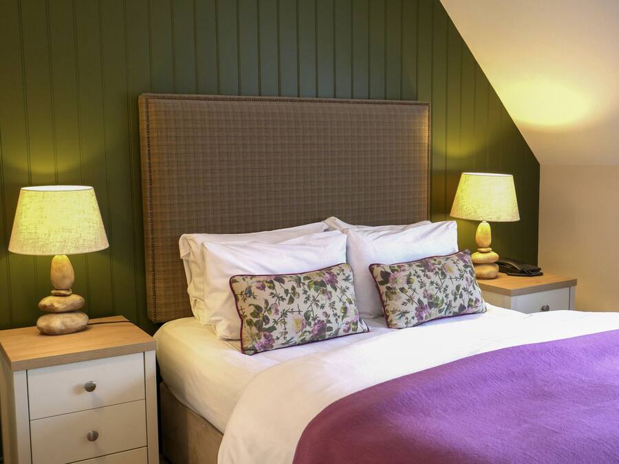 A neatly made bed with white linens and two floral pillows, flanked by two bedside tables with lamps and a phone.