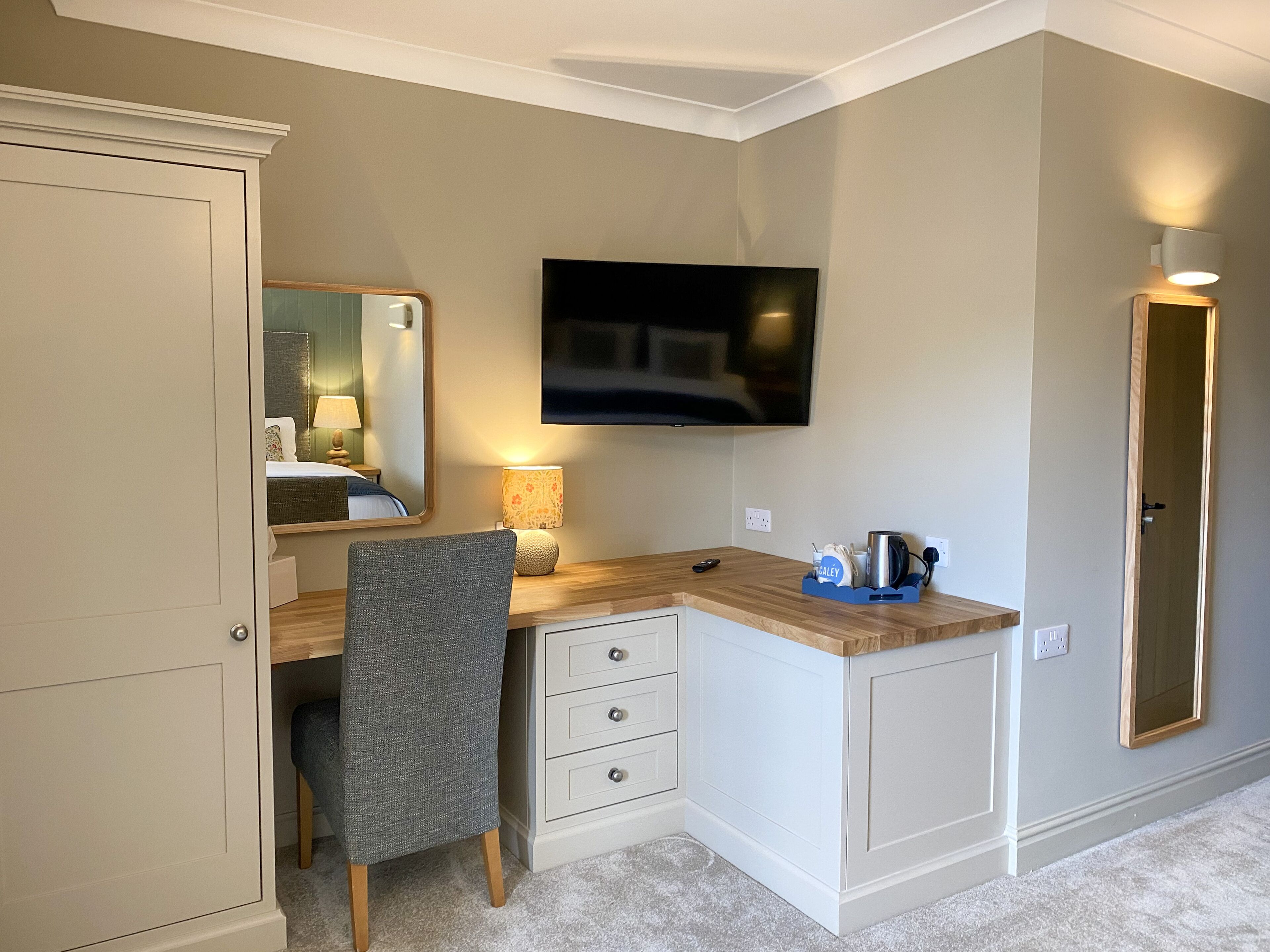 A compact hotel room with a desk, chair, television, and a small kitchenette area.