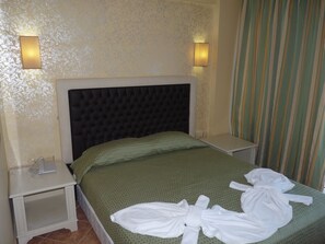 Une chambre d’hôtel avec une tête de lit capitonnée, une couvre-lit verte, deux lampes de chevet et un rideau à rayures.