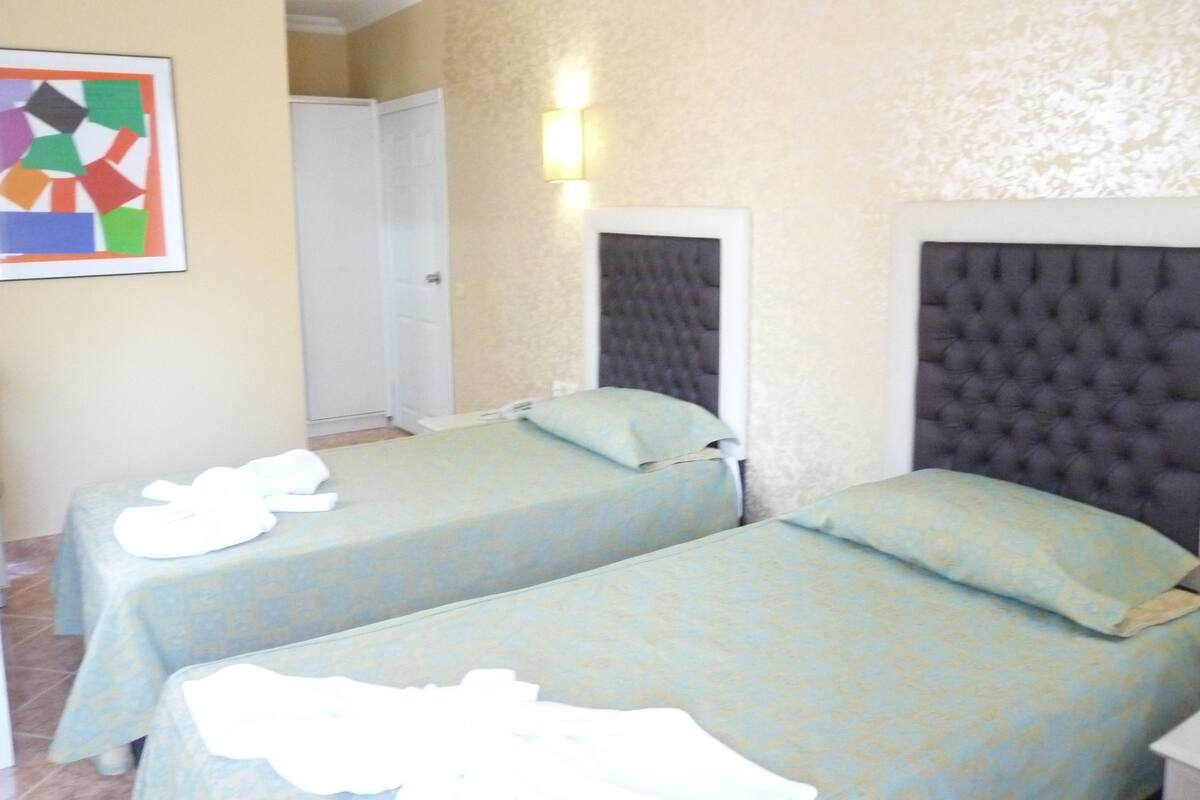 Une chambre d’hôtel avec deux lits, une porte et un luminaire fixé au mur.