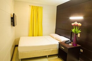 A small, neatly arranged hotel room with a bed, bedside table, and a vase with flowers. - Sulit Place (Quezon City)
