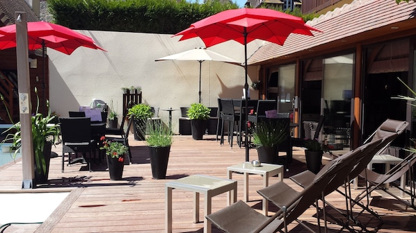 Eine Terrassengruppe im Freien mit Holzboden, schwarzen und braunen Lounge-Stühlen und roten Sonnenschirmen.