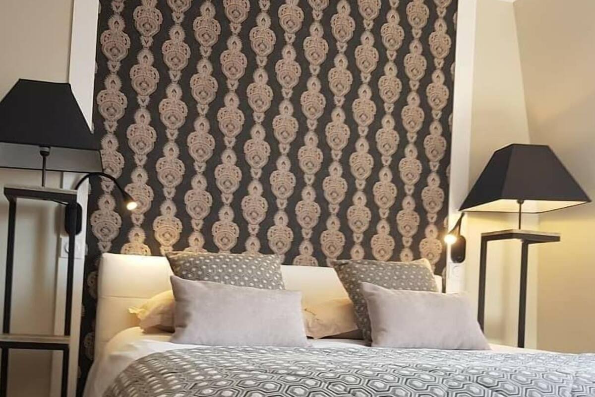 Una cama bien hecha con ropa de cama estampada, dos lámparas de noche y un papel tapiz con diseño.