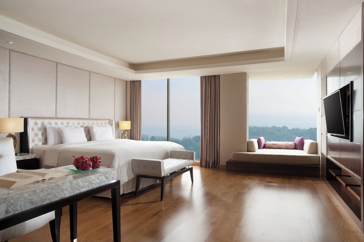 A hotel room with a large bed, a desk with a chair, a sofa, a TV, and a view of the outdoors.