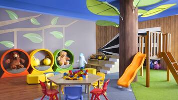 Zona de juegos infantiles con tobogán, estructuras recreativas y asientos coloridos.