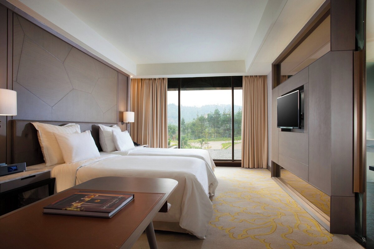 A hotel room with a bed, a desk, a TV, and a view of the outdoors.