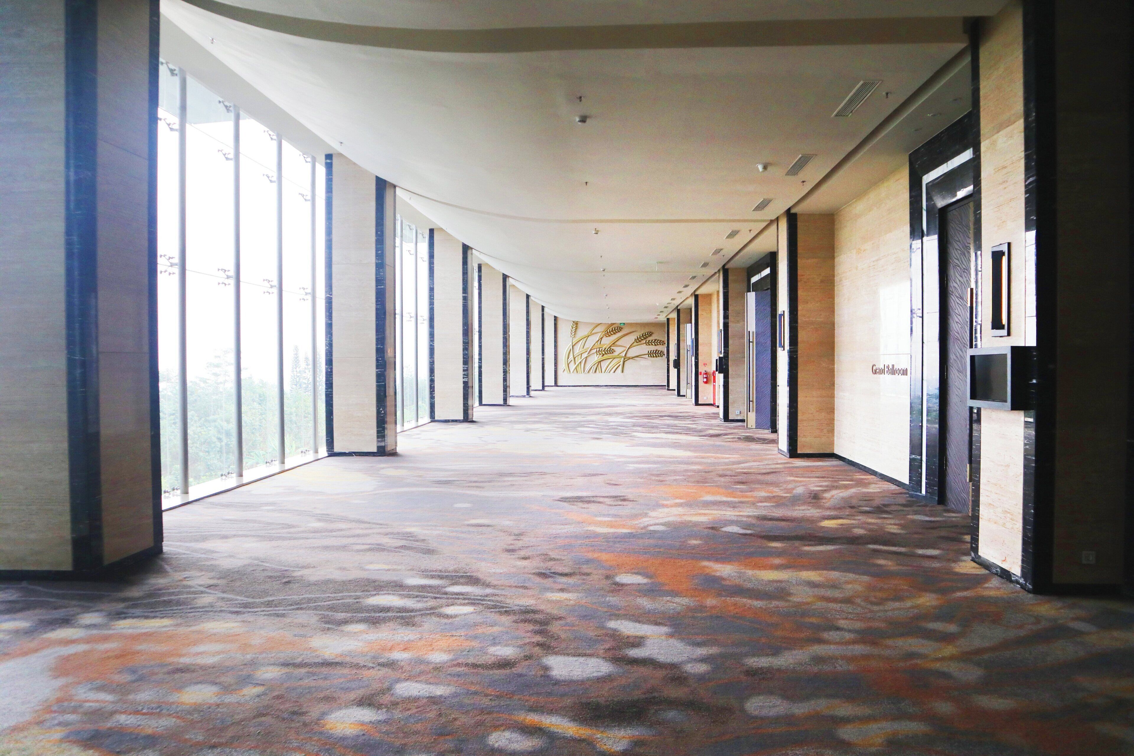 A long corridor with large windows on one side and doors on the other, leading to a Grand Ballroom.