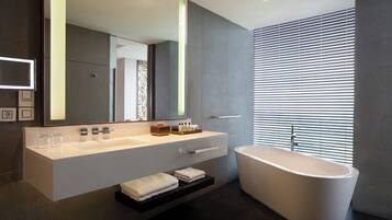 Un baño moderno con una bañera independiente grande, un lavabo con espejo y una ventana con persianas.