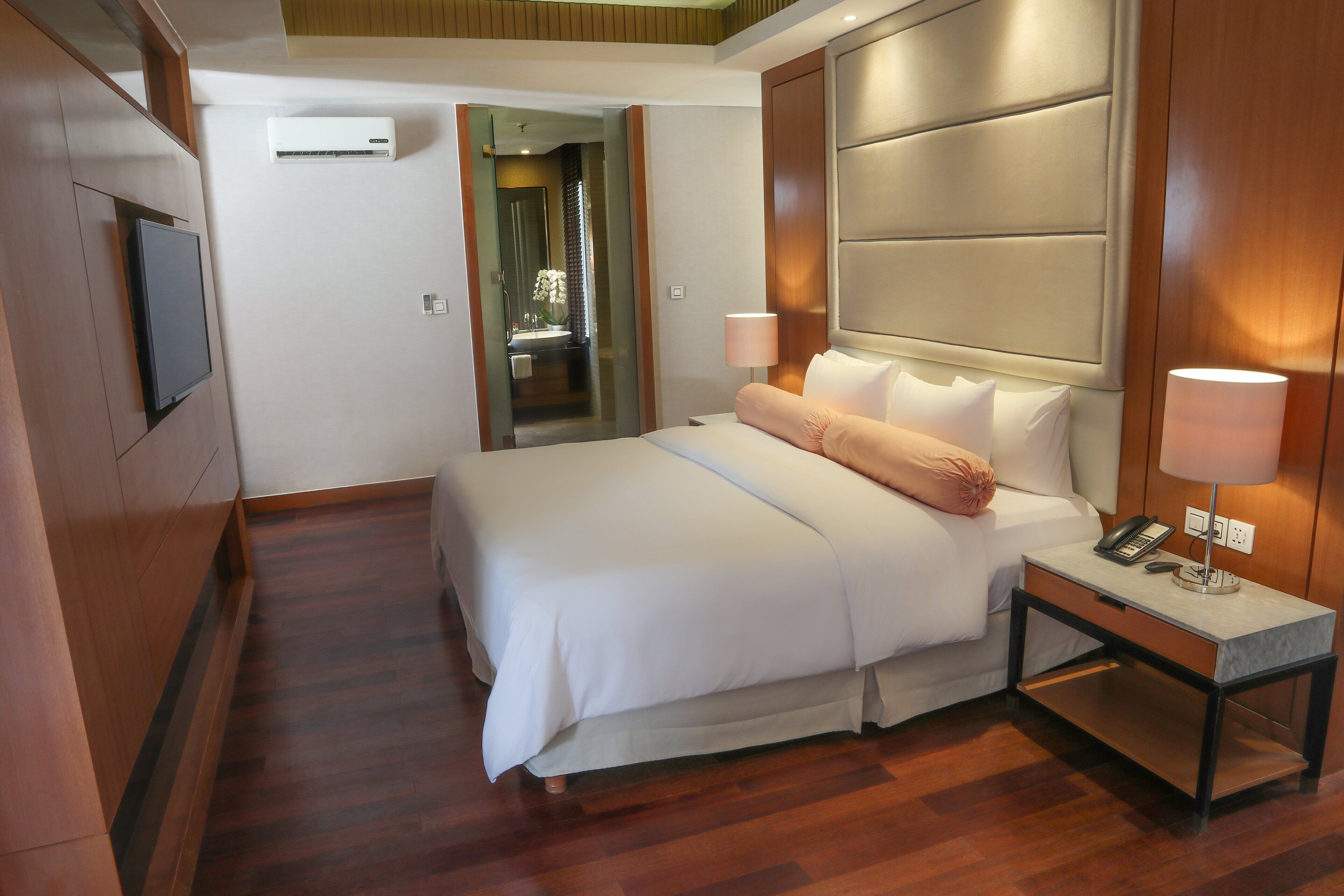 A hotel room with a bed, bedside table, lamp, and a television mounted on the wall.
