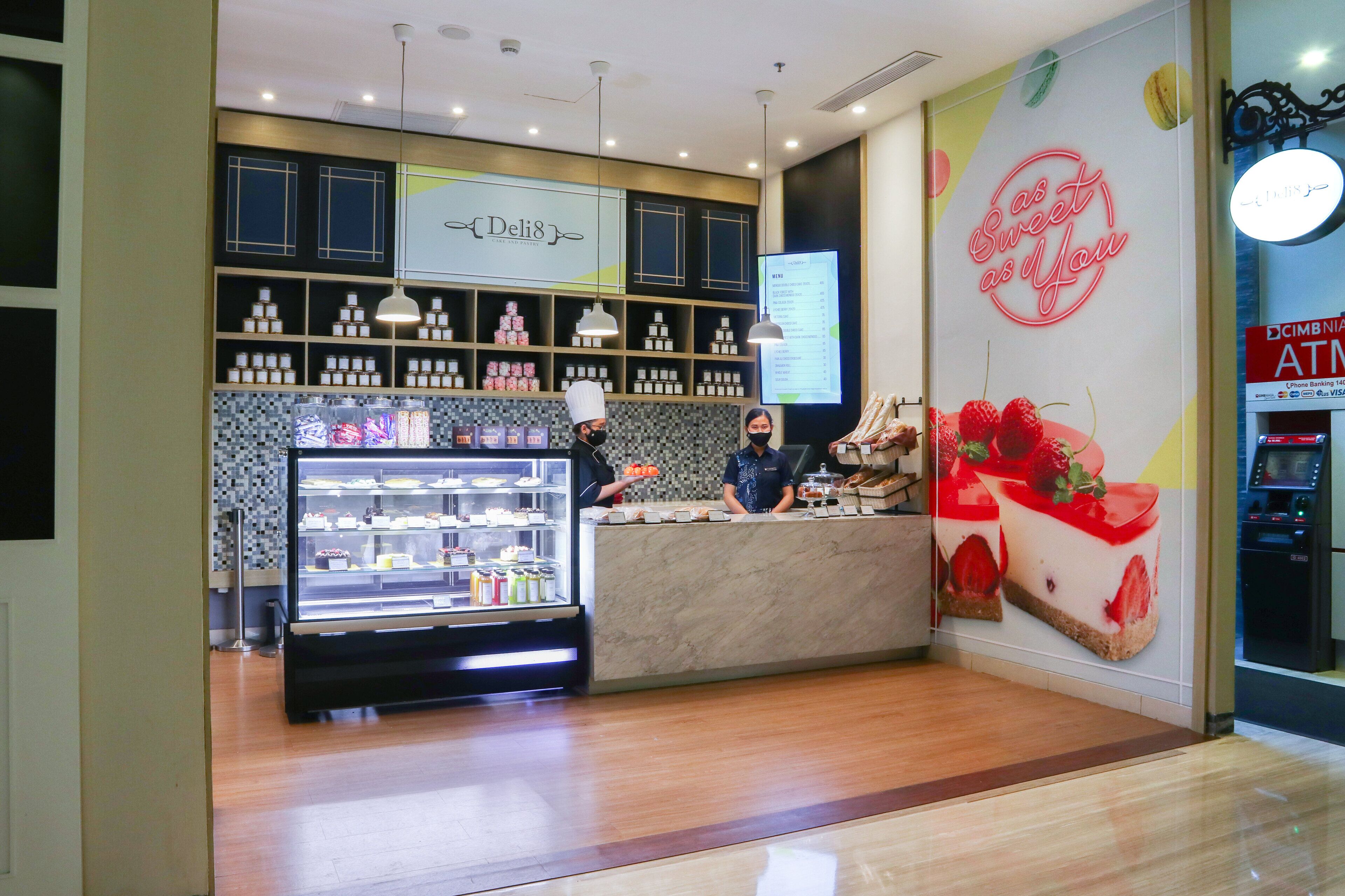 A deli counter with a refrigerated display case, a menu board, and a wall advertisement.