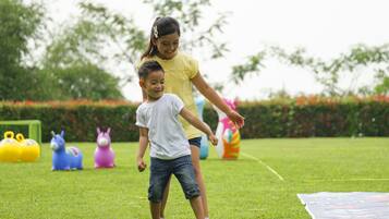 Un niño y un adulto en un espacio al aire libre con césped, un seto y árboles al fondo.