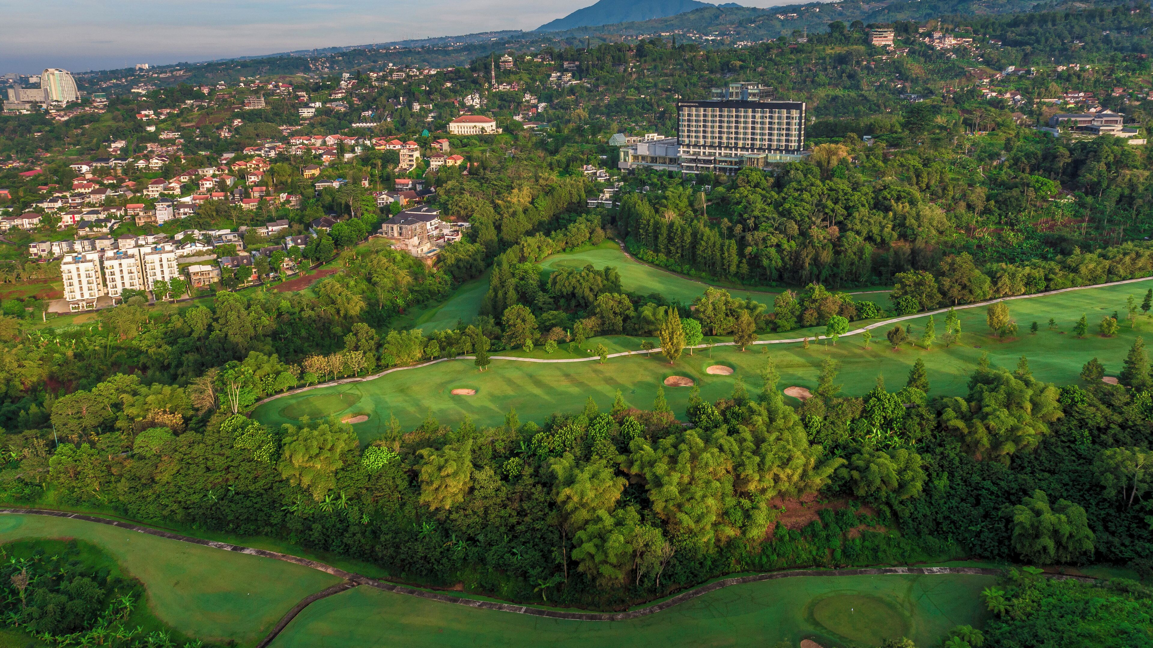 Vue aérienne d’un terrain de golf, avec un grand bâtiment et une zone résidentielle en arrière-plan.