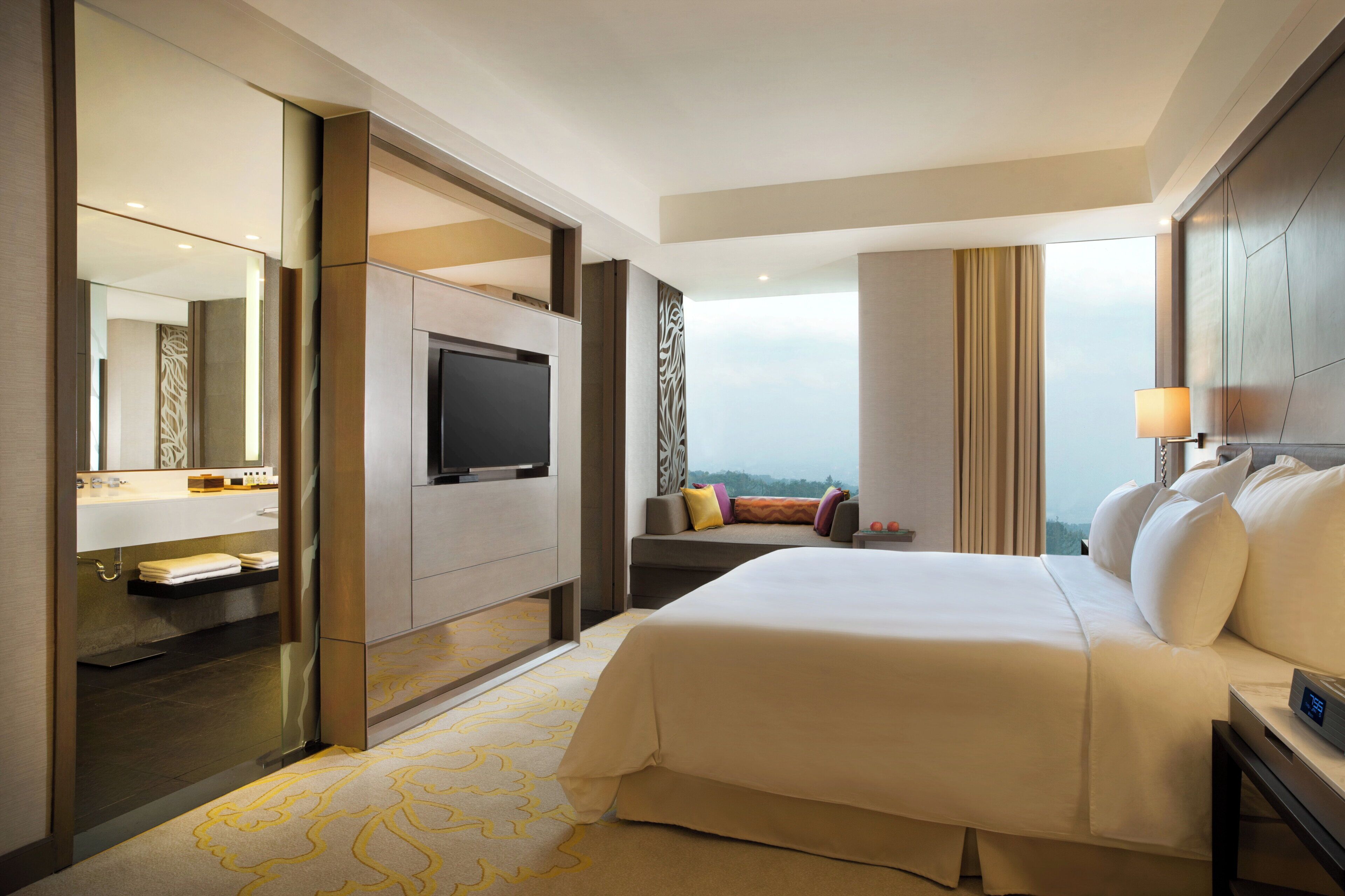 Ein Hotelzimmer mit Bett, Fernseher, Sofa und Blick auf die Stadt.