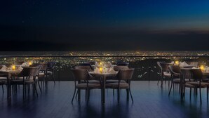 A rooftop dining area with wicker tables and chairs, candles, and a cityscape view at night. - InterContinental Bandung Dago Pakar by IHG (Cimenyan)