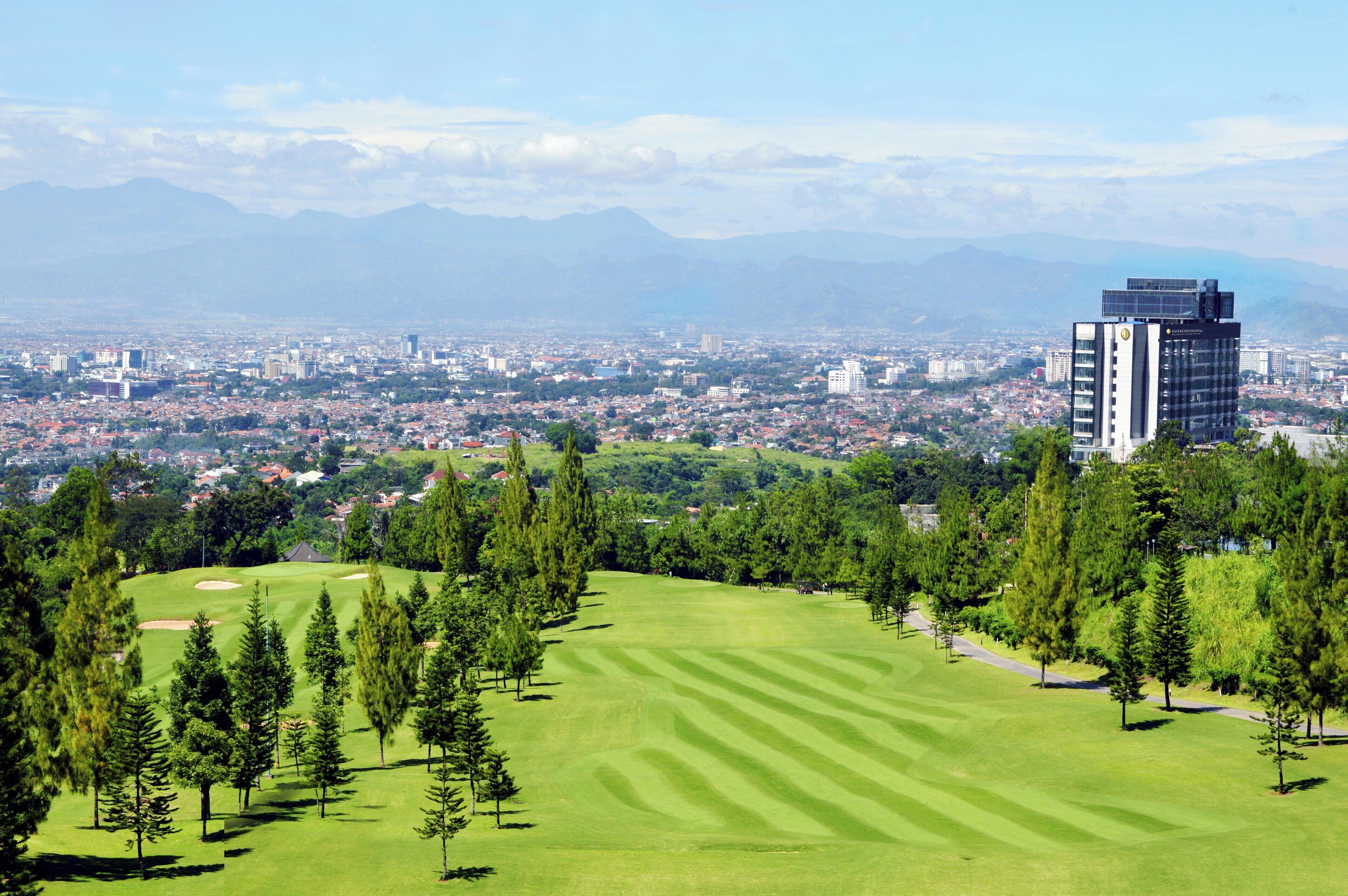 Un campo de golf con un paisaje urbano y montañas al fondo.
