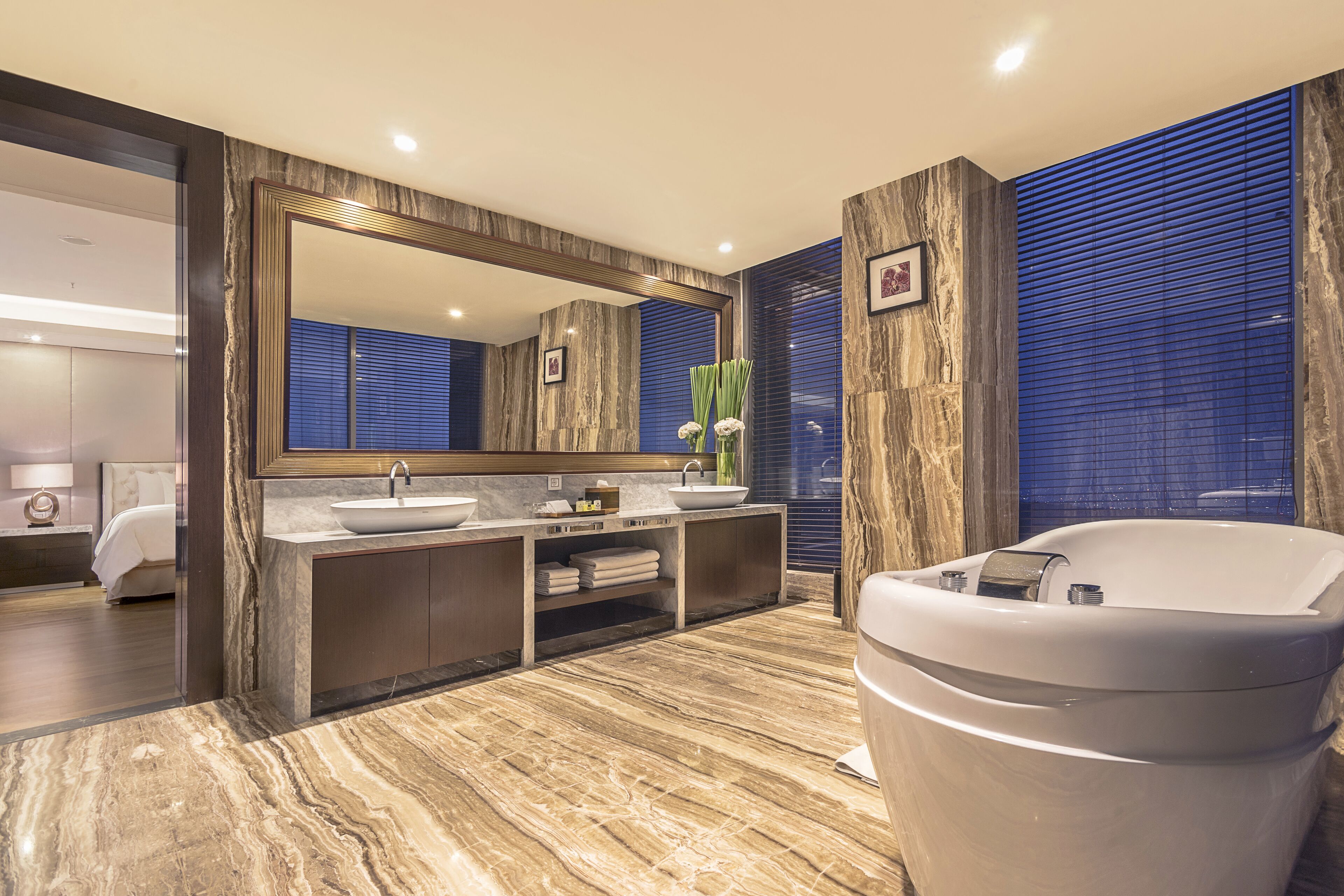 A modern bathroom with a large mirror, two sinks, a bathtub, and marble flooring.