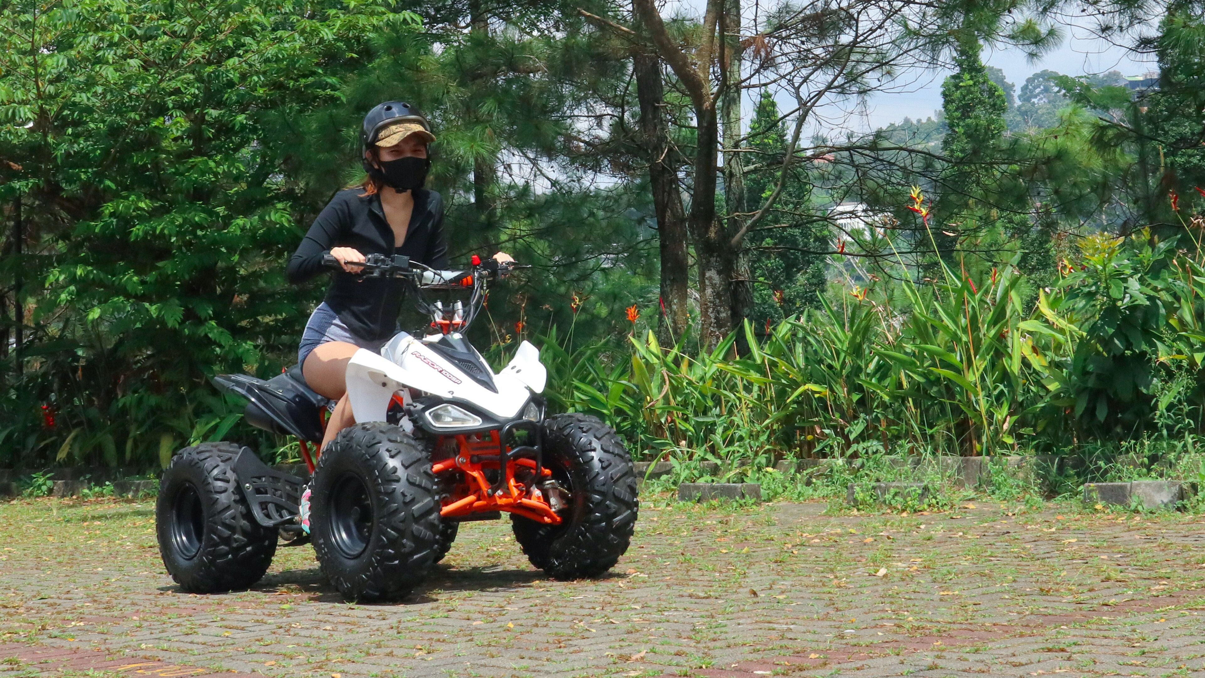 A person riding a quad bike on a paved path surrounded by lush greenery and trees.