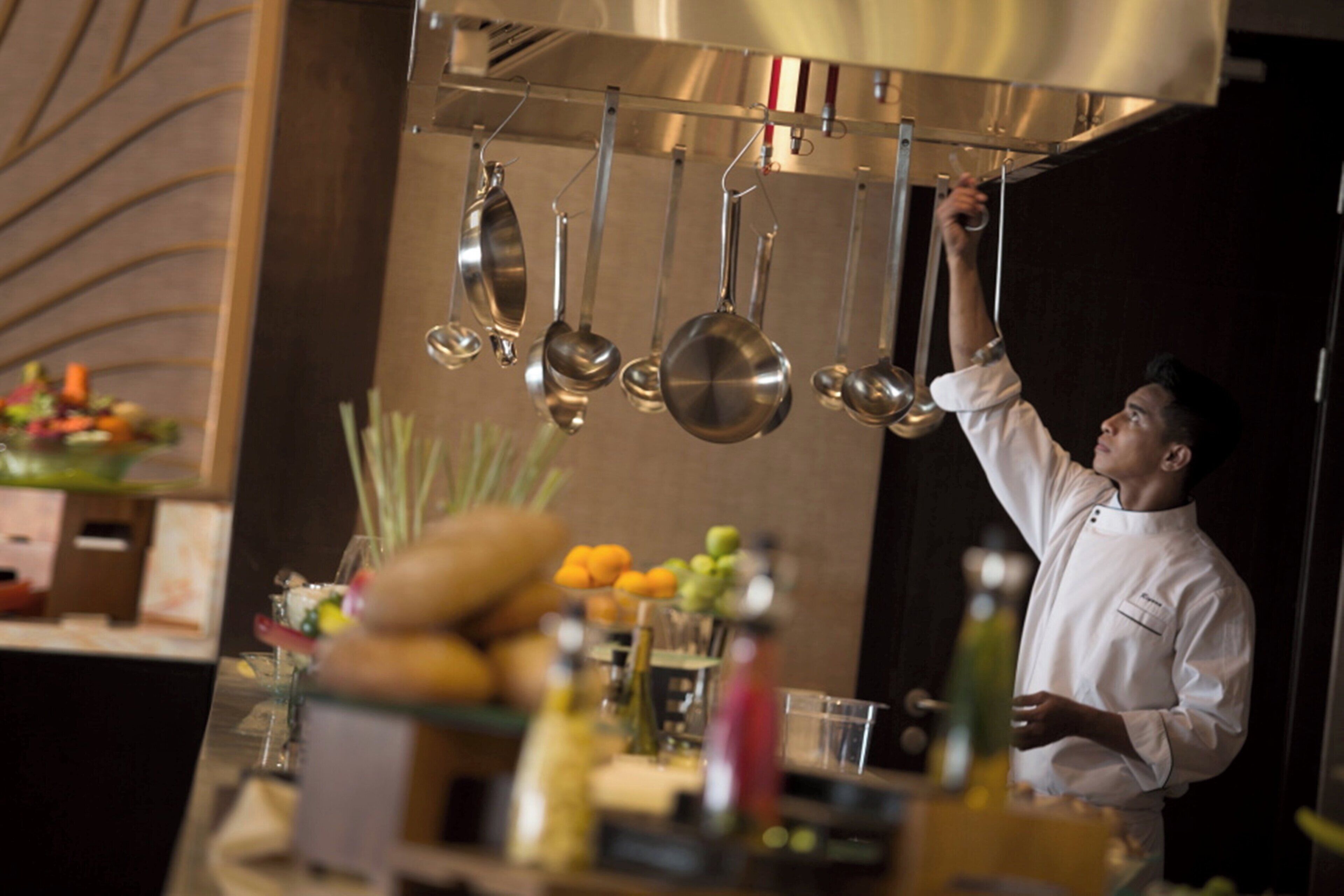 Un chef alcanzando una olla de un colgador en una cocina.