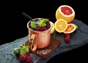 A copper mug with a black straw, filled with a dark beverage, garnished with mint leaves and berries, on a slate surface with a 'VINTAGE' label. - Wyndham Grand Shenzhen (Shenzhen)