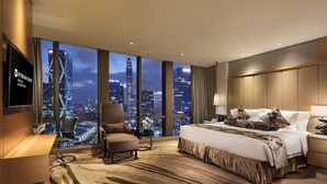 Habitación de hotel con una cama grande, un escritorio, una silla y un televisor. La habitación tiene vista a un horizonte urbano de noche.
