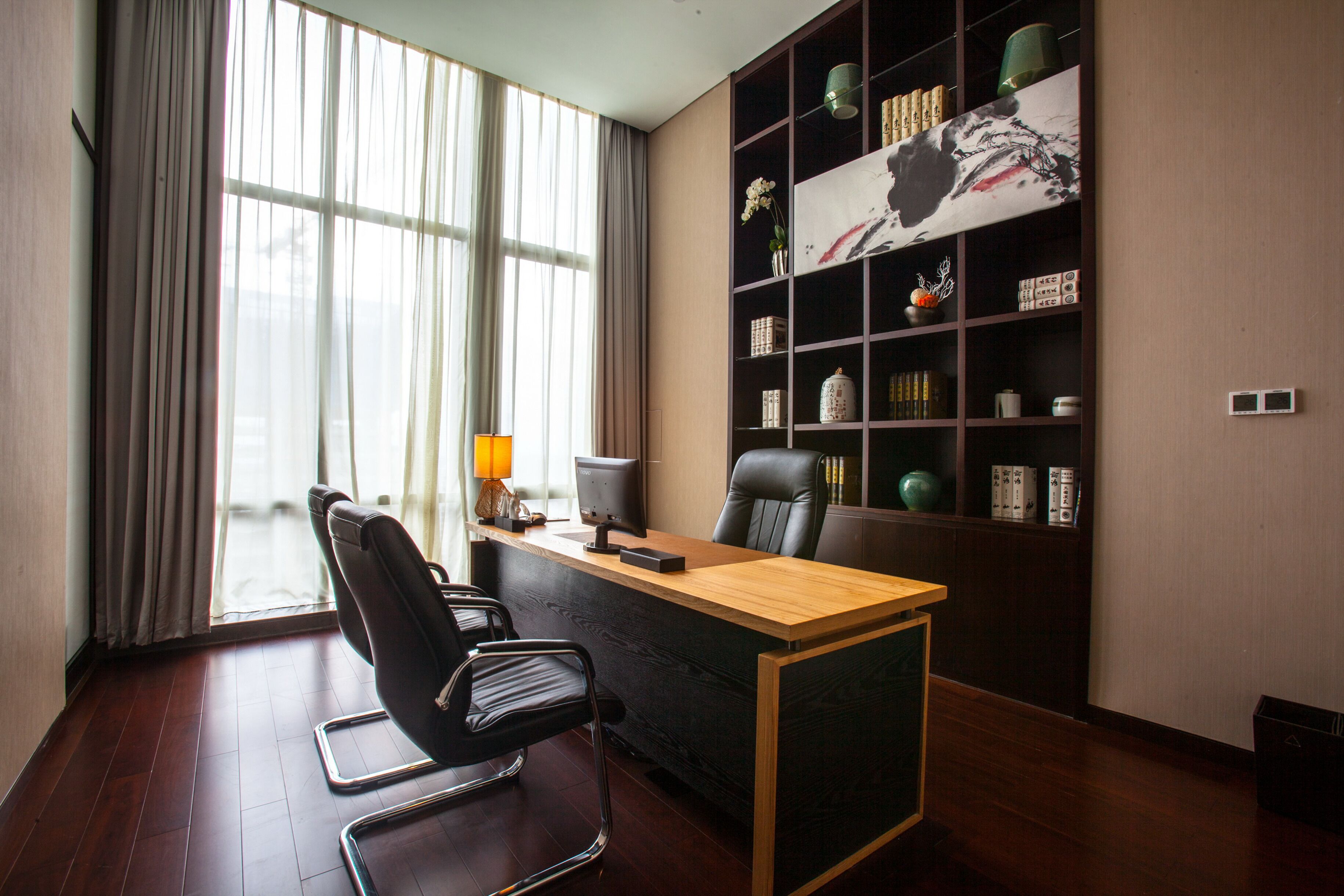A modern office with a wooden desk, black office chair, and a large bookshelf.