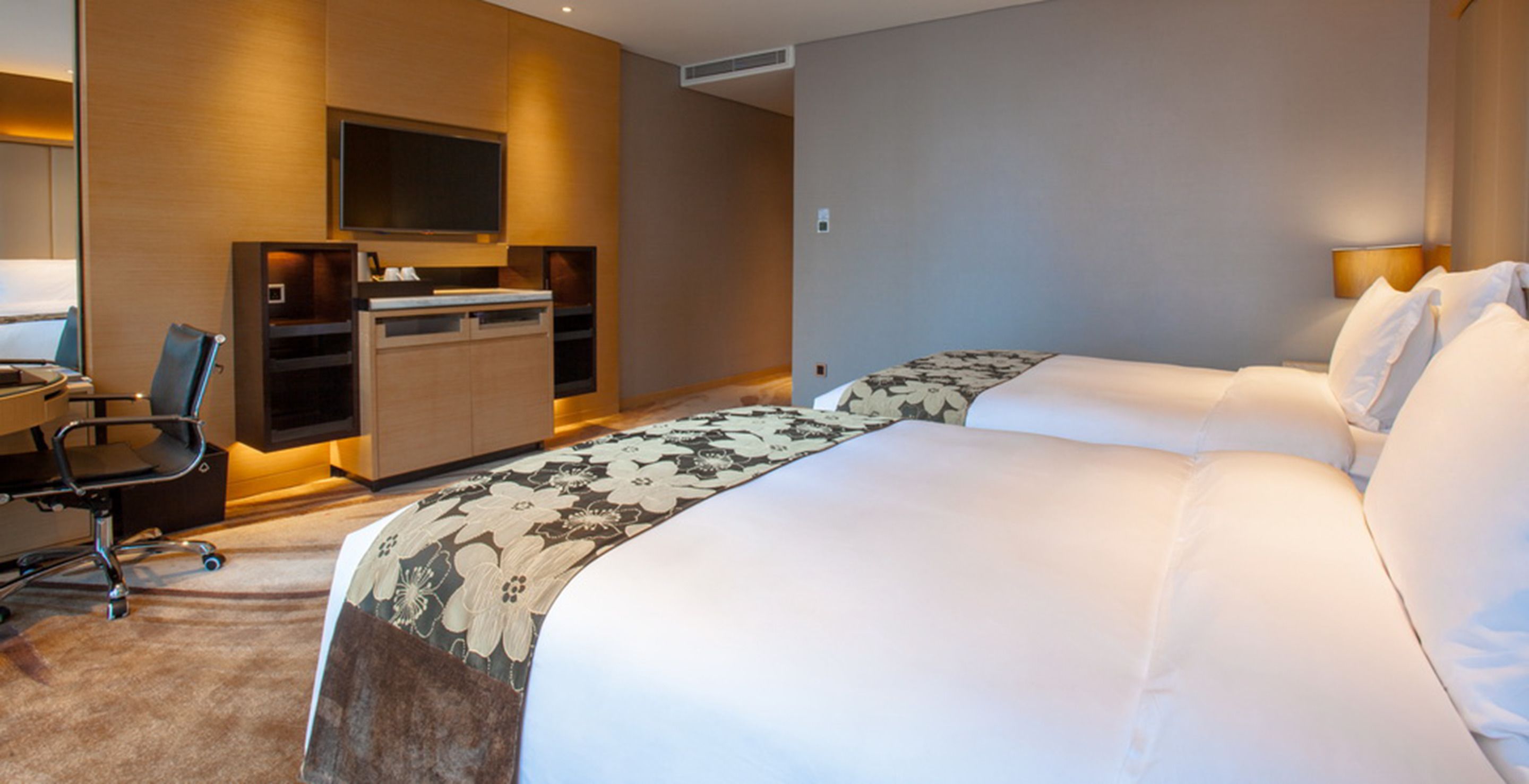 A hotel room with two beds, a desk, a chair, and a television.