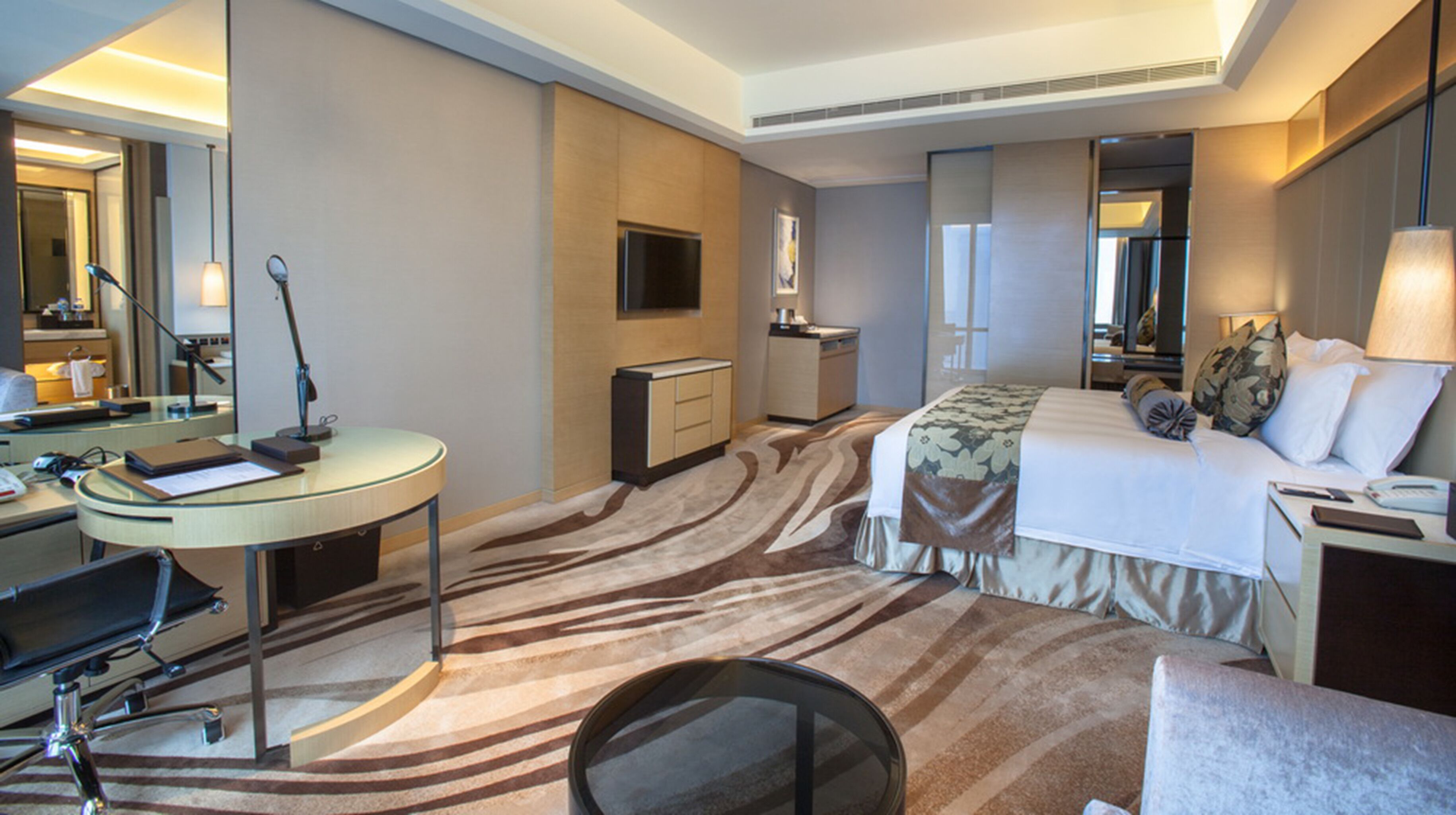Ein Hotelzimmer mit Bett, Schreibtisch, Stuhl, Fernseher, Spiegel und einem Teppich mit Zeprazebra-Muster.