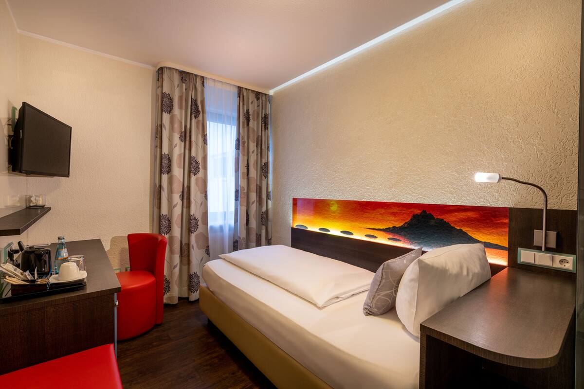 Habitación de hotel con cama, escritorio, silla, televisión y un cuadro de un atardecer.