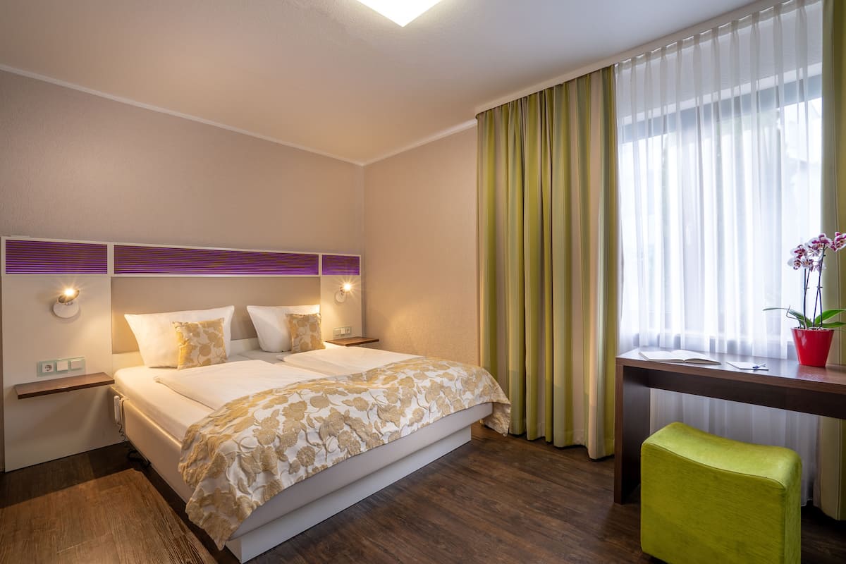 Una habitación de hotel con cama, mesitas de noche, un escritorio, una silla y una ventana con cortinas.