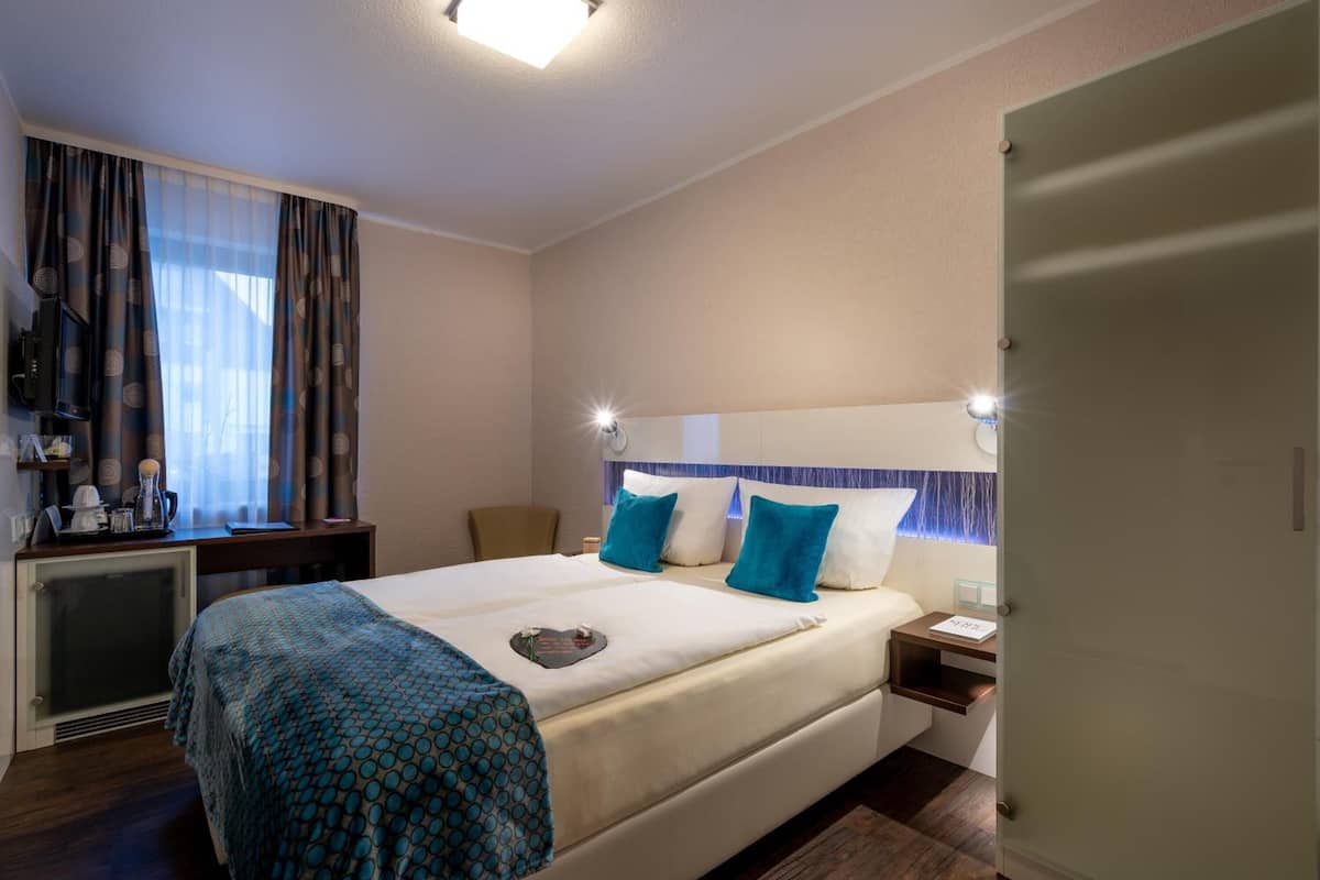 Habitación de hotel con cama, mesitas de noche, escritorio con silla, armario y ventana con cortinas.