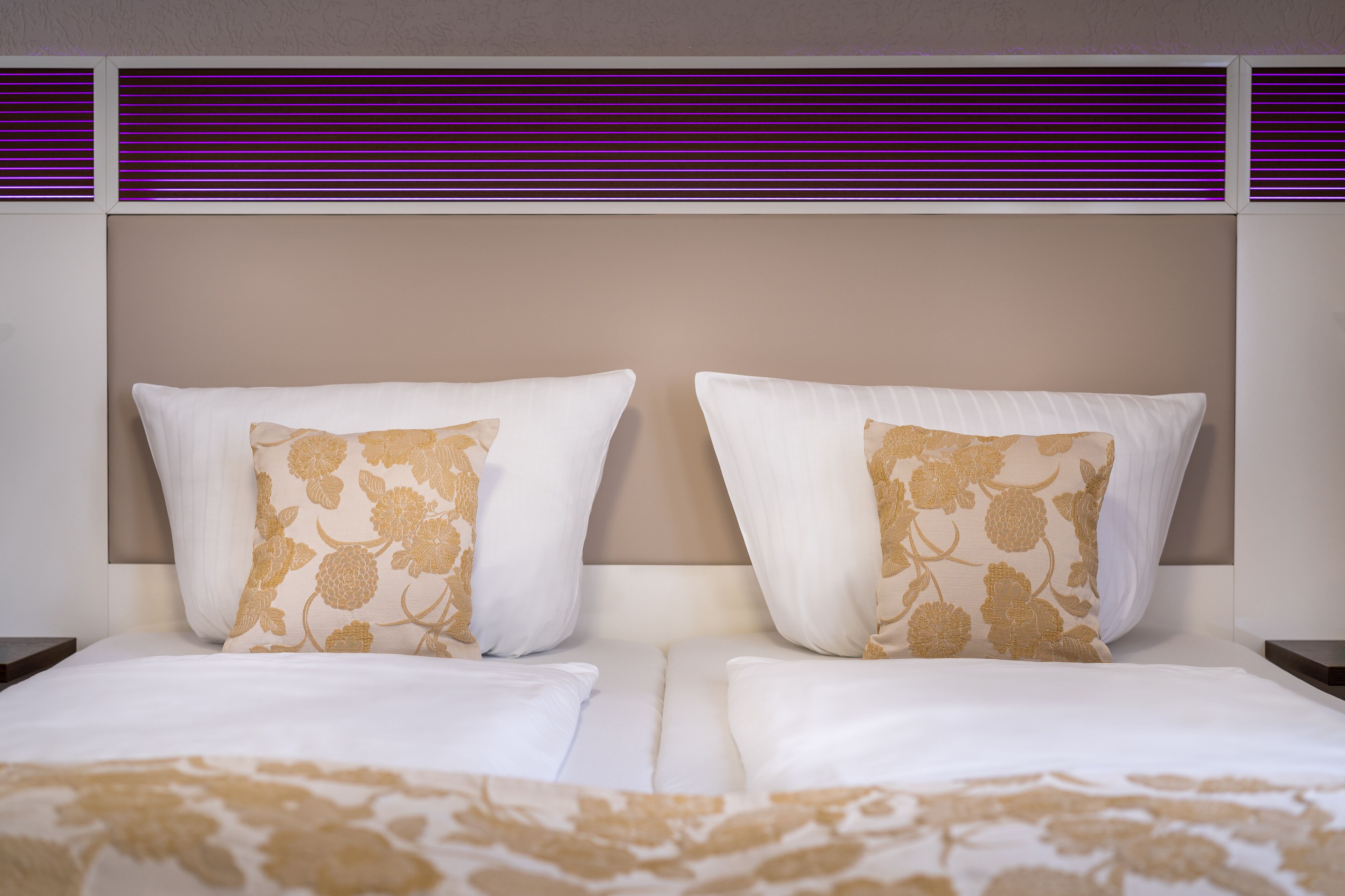 A hotel room with two beds, each with white linens and floral-patterned pillows.