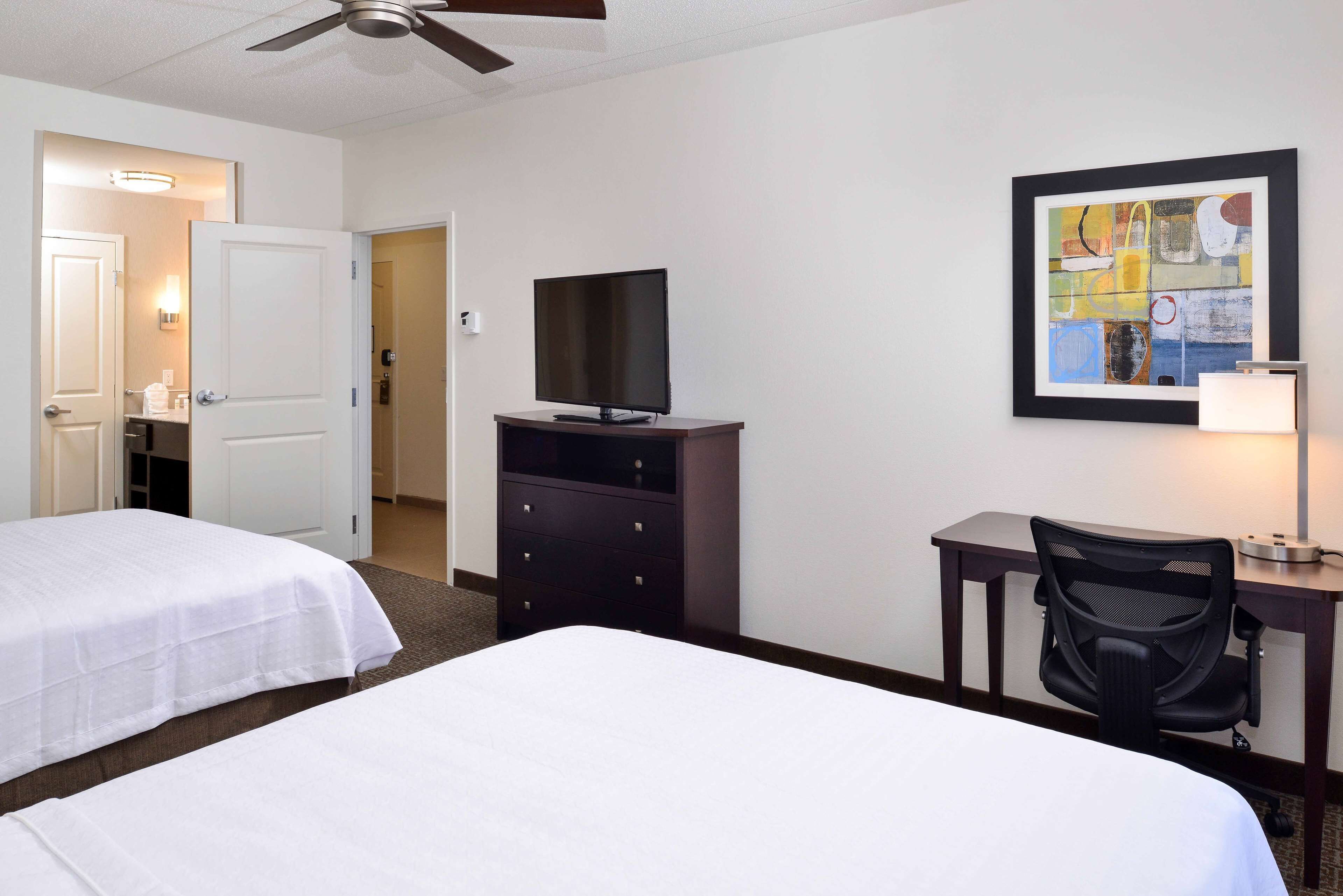 A hotel room with two beds, a desk with a chair, a television, and a framed artwork on the wall.