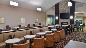 A hotel lobby with a seating area, tables, a fireplace, and a TV mounted on the wall. - Homewood Columbia Laurel (Laurel)