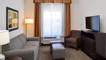 Habitación de hotel con sofá, sillón, otoman, televisor y lámpara.