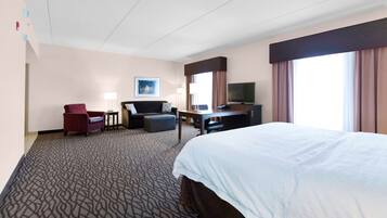 A hotel room with a large bed, a desk with a chair, a sofa, a TV, and a window with curtains.
