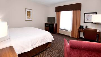 Une chambre d’hôtel avec un lit, un bureau avec un ordinateur, une télévision et une chaise.