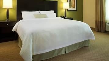 A neatly made bed with white linens in a hotel room with green walls and a dark headboard.