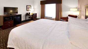 A hotel room with a large bed, a desk with a computer, a television, and a window with curtains.