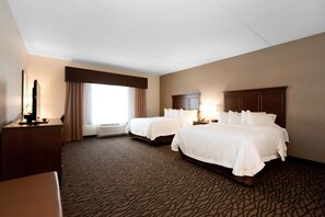 A hotel room with two beds, a desk, a TV, and a window with curtains.