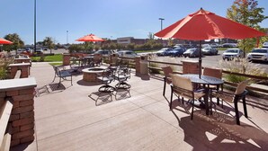 An outdoor patio area with tables and chairs, red umbrellas, and a brick wall. - Hampton Inn Butler (Butler)