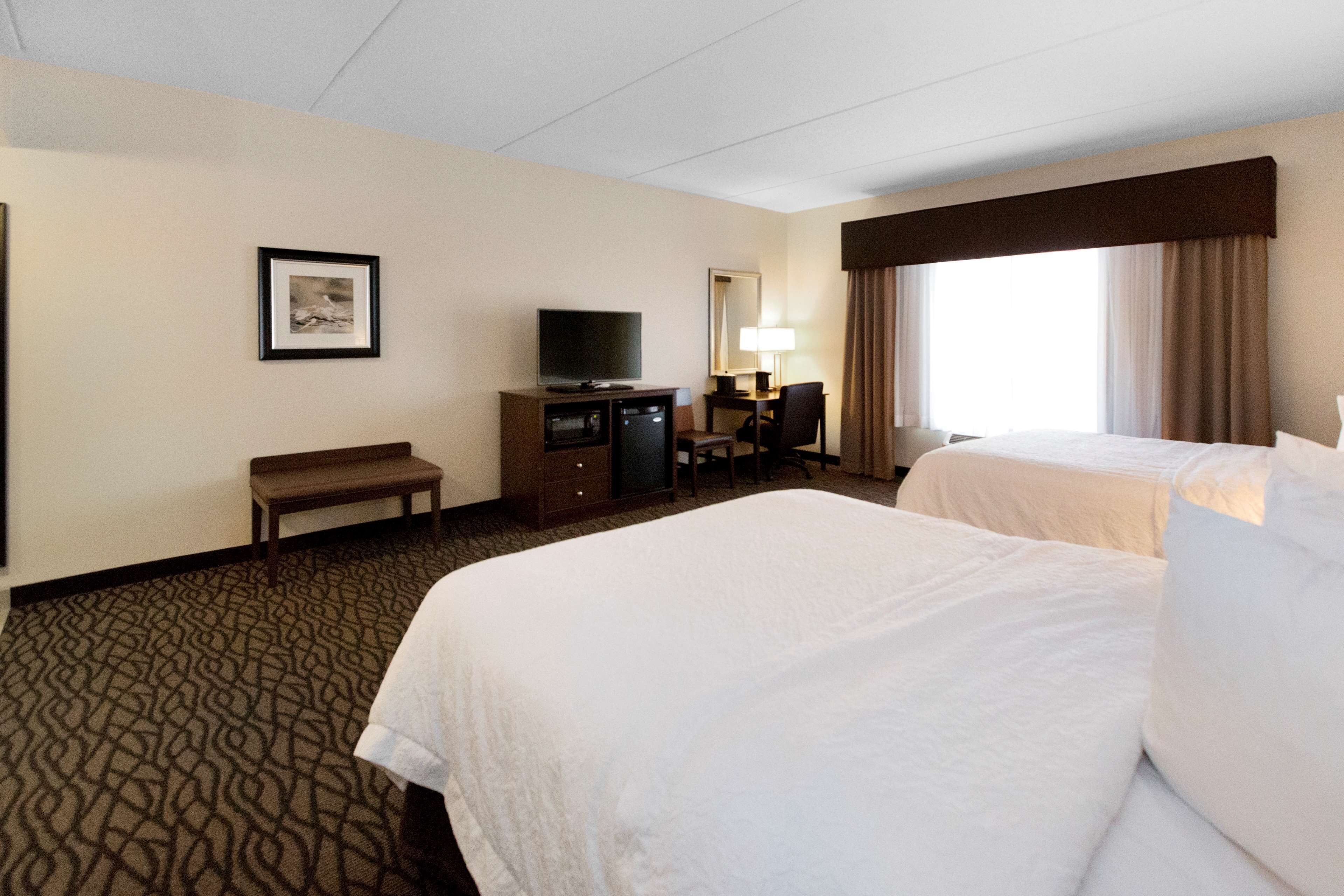 A hotel room with two beds, a desk, a television, a lamp, and a framed picture on the wall.
