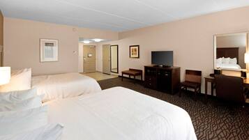 Quarto de hotel com duas camas, uma televisão, uma escrivaninha, uma cadeira e um espelho.