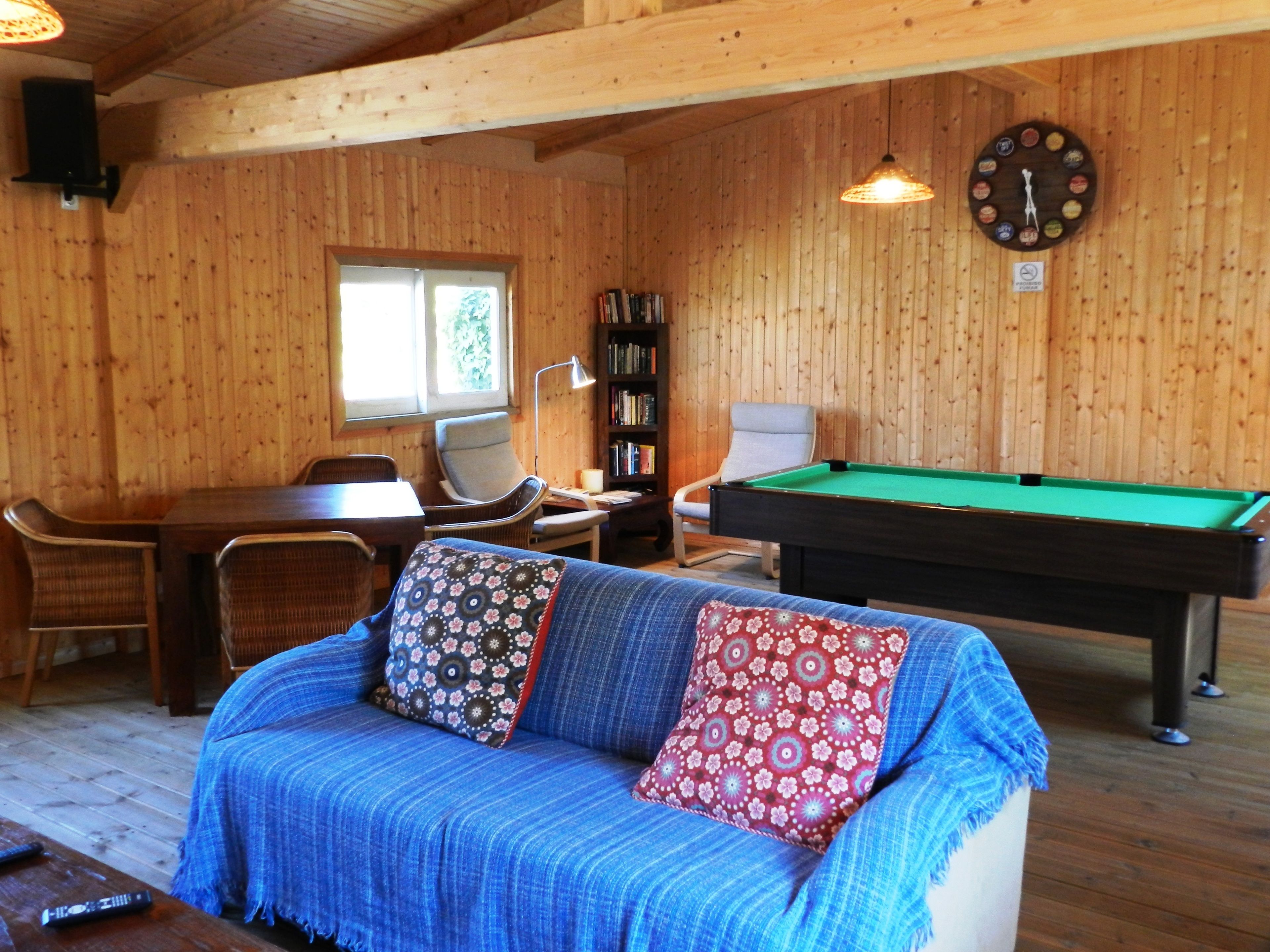 A cozy room with a pool table, a sofa with patterned cushions, a bookshelf, and a clock on the wall.