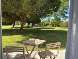 An outdoor seating area with a wooden table and two chairs, surrounded by trees and a grassy lawn.