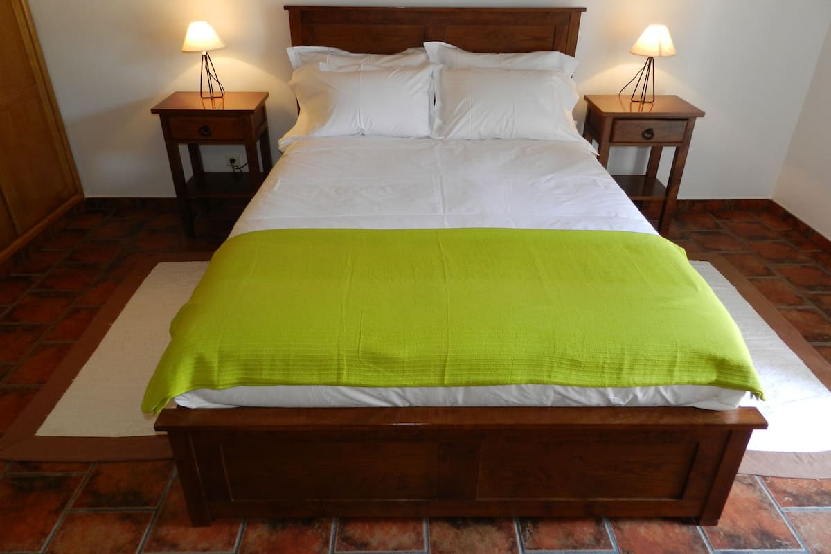 A neatly made bed with a wooden headboard, two bedside tables with lamps, and a green throw blanket.