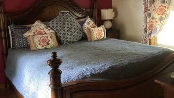 Un dormitorio con cama de madera, cortinas florales, ventilador de techo y ventana con cortinas estampadas.