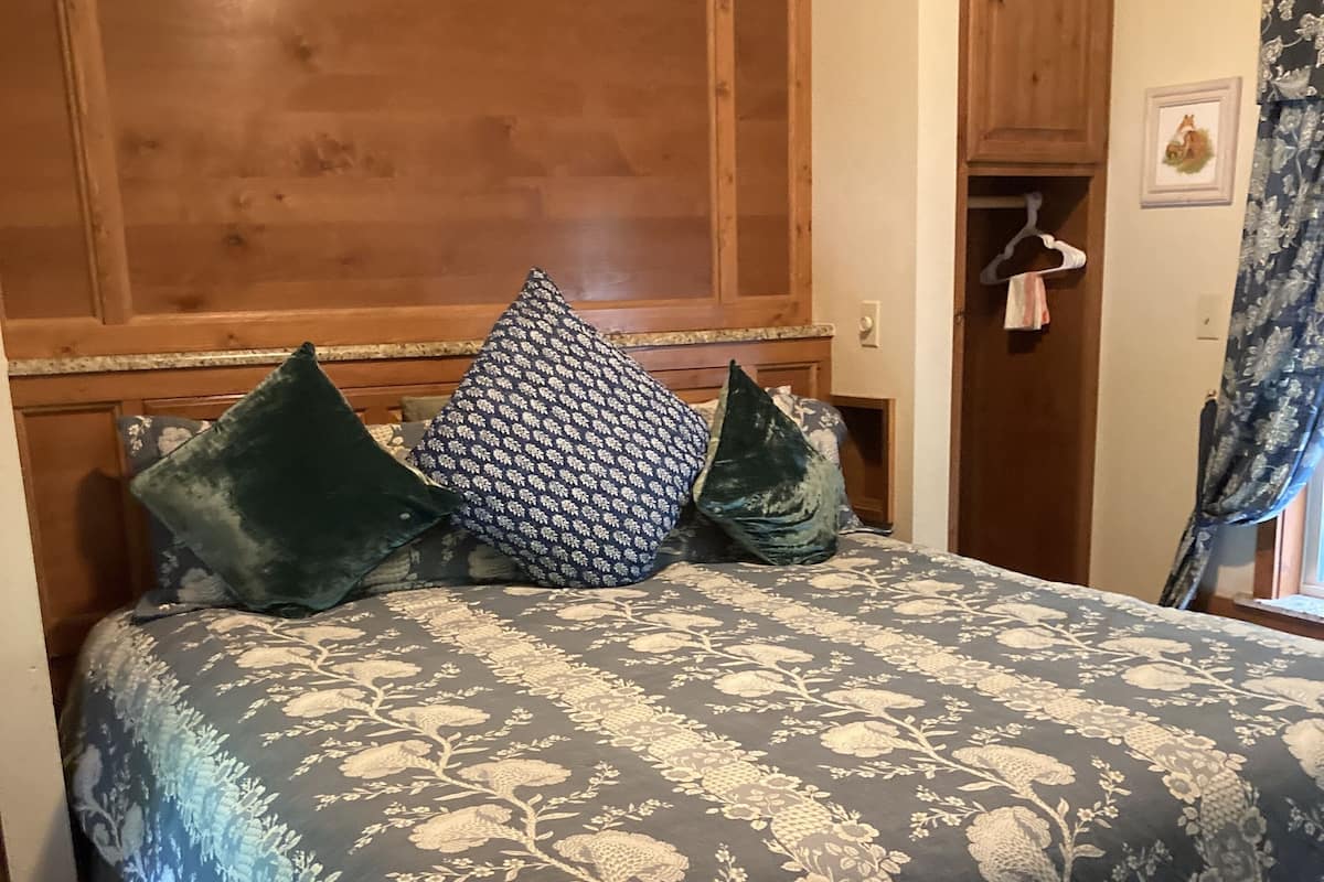A bedroom with a wooden headboard, a floral-patterned bedspread, and a wooden wardrobe.